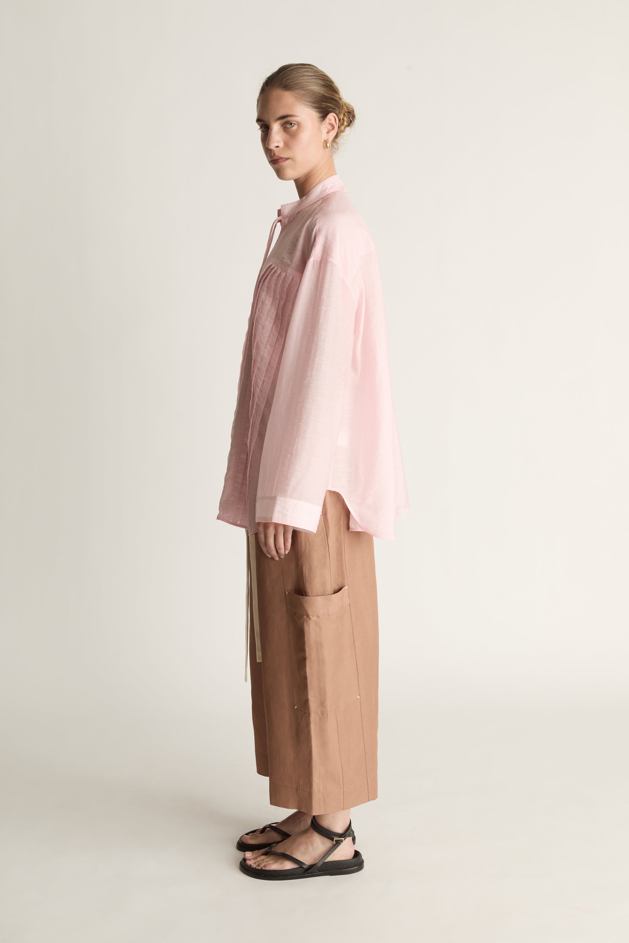 Person wearing a light pink shirt and brown pants on a white background