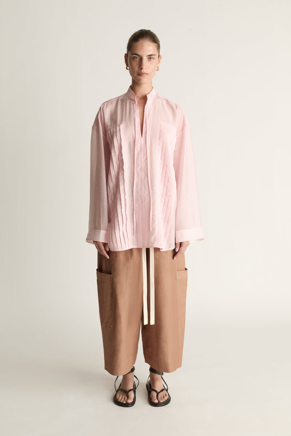 Person wearing a light pink shirt and brown pants on a white background