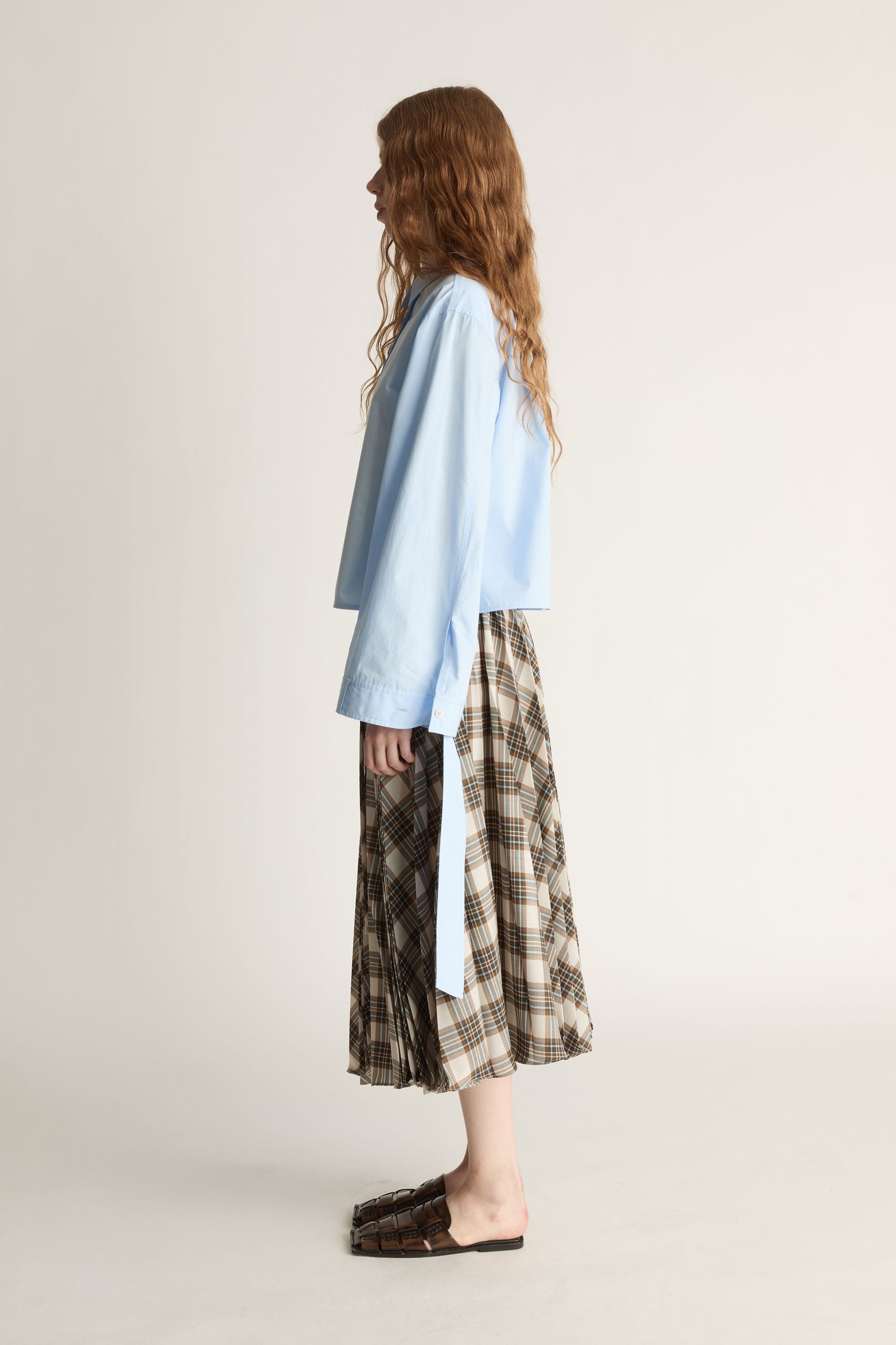 Woman wearing a light blue shirt and plaid skirt on a plain background