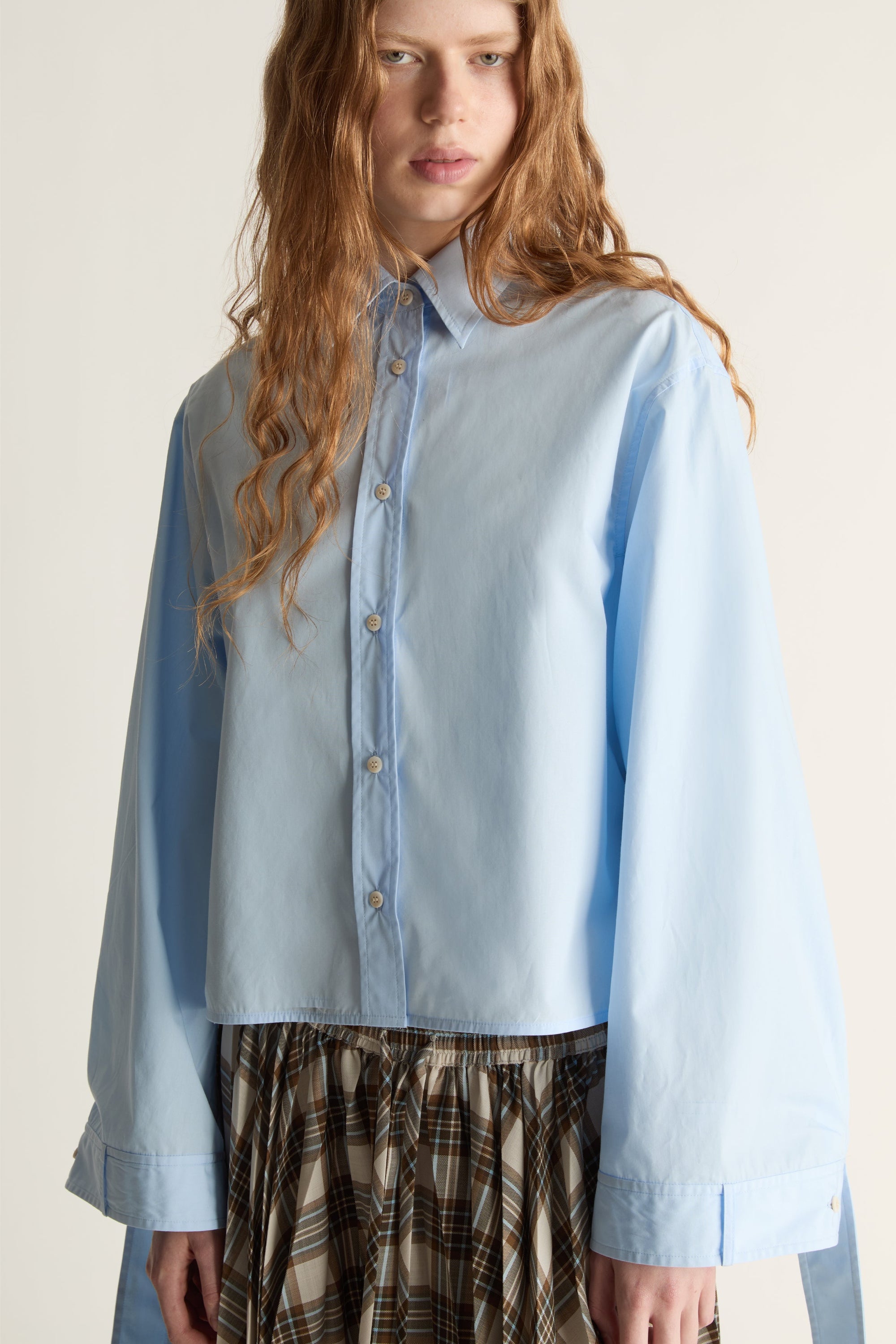 Woman wearing a light blue shirt and plaid skirt on a plain background