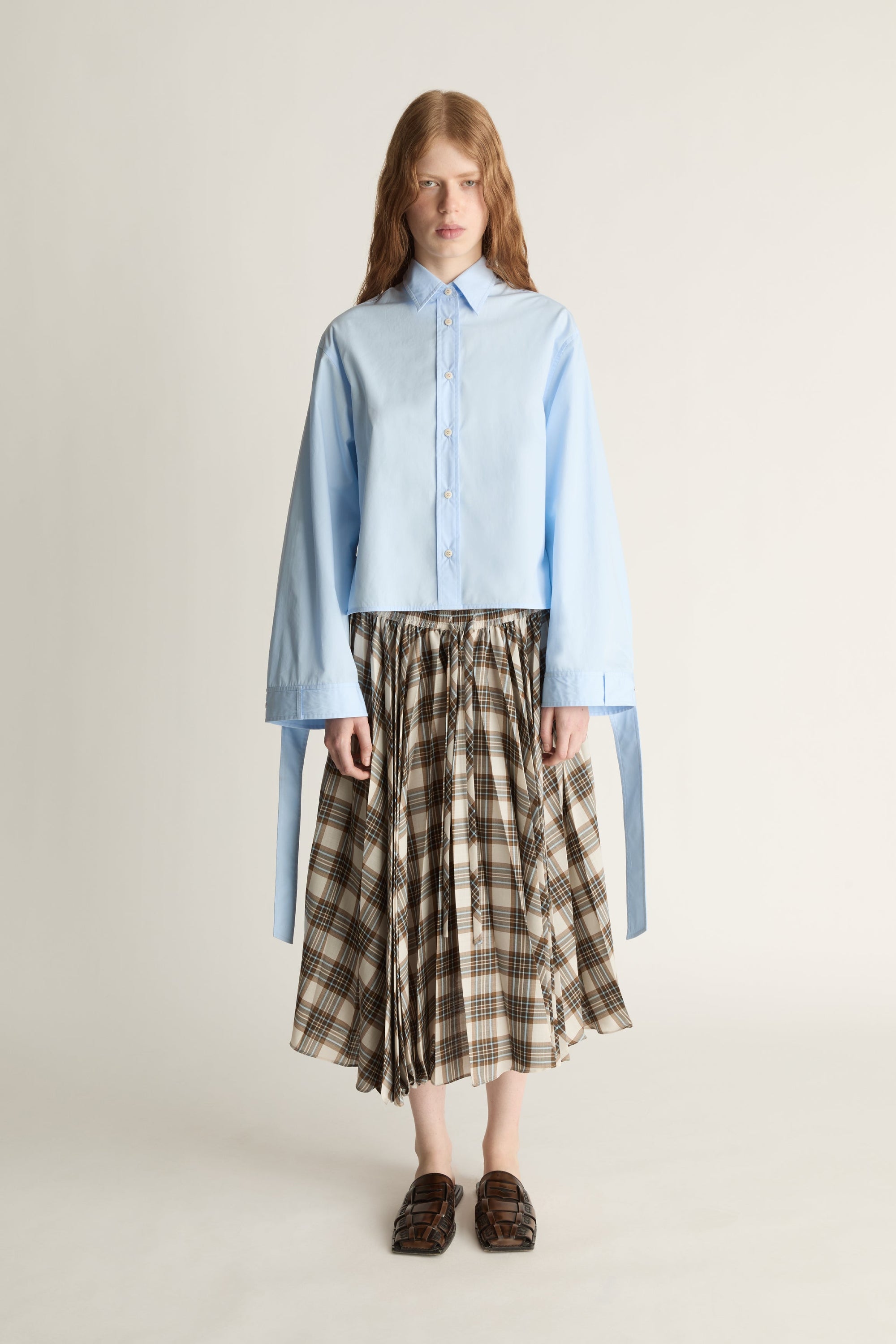 Woman wearing a light blue shirt and plaid skirt on a plain background
