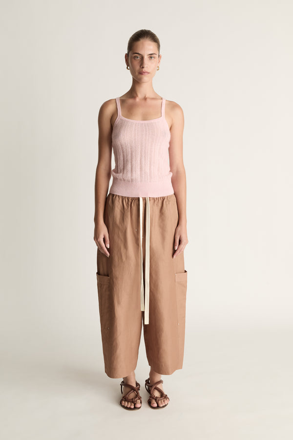Woman wearing a pink top and brown pants on a white background