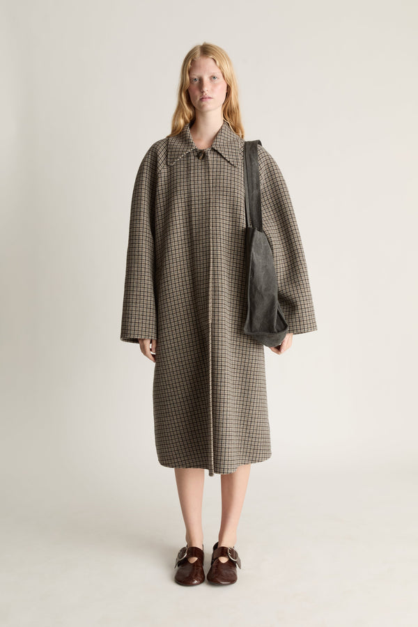 Person wearing a long checkered coat holding a bag on a plain background