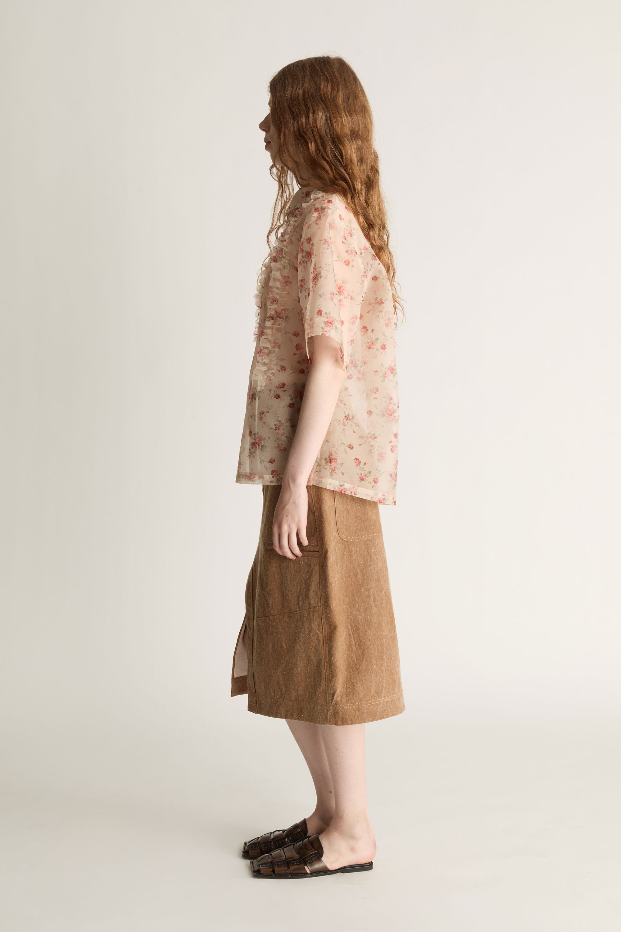 Person wearing a floral blouse and brown skirt on a white background