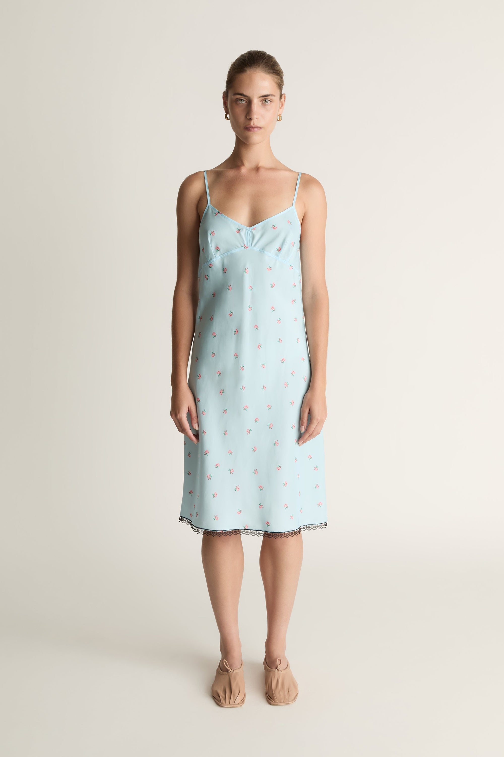 Woman wearing a light blue slip dress with a subtle pattern on a plain background