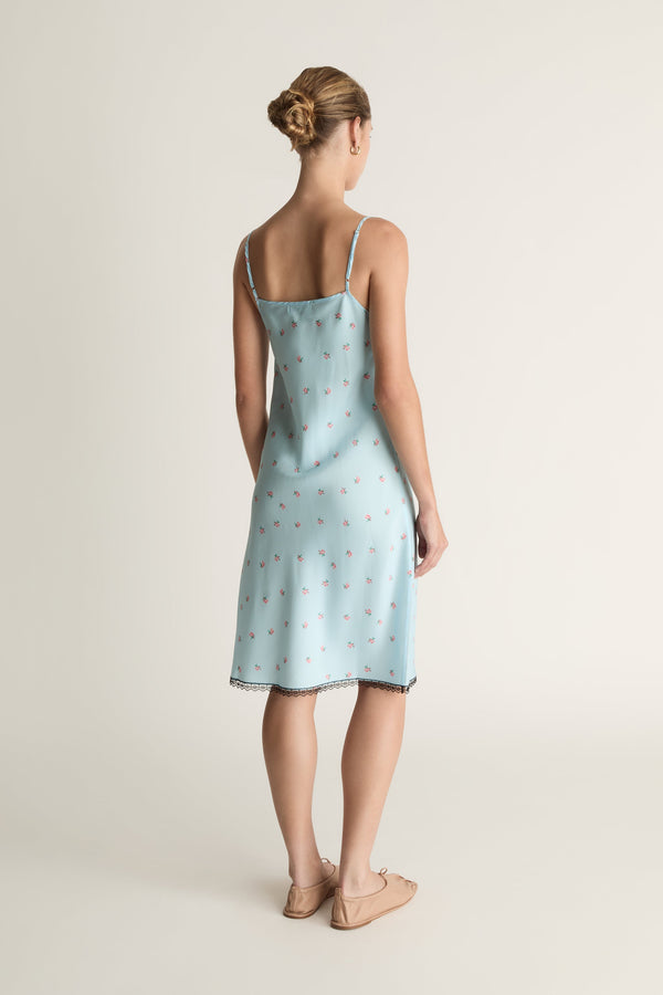 Woman wearing a light blue slip dress with a subtle pattern on a plain background