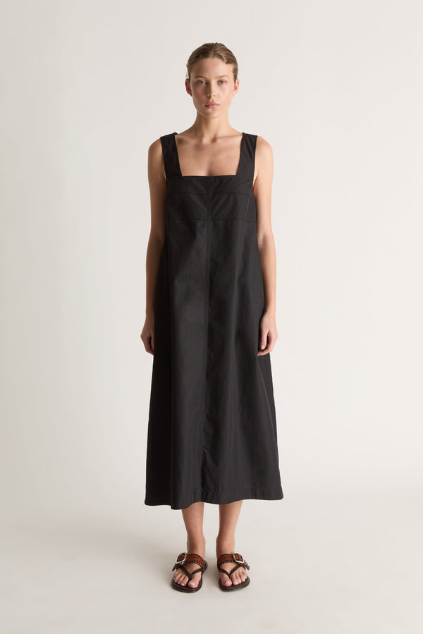 Front view of a black A-line midi dress with a square neckline, wide straps and topstitched yoke seams.