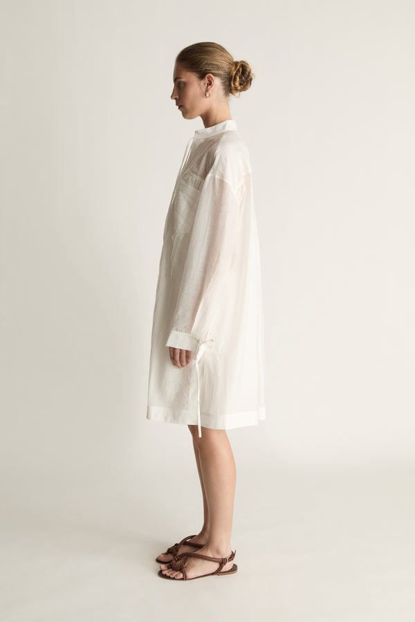 Woman wearing a white tunic against a plain background