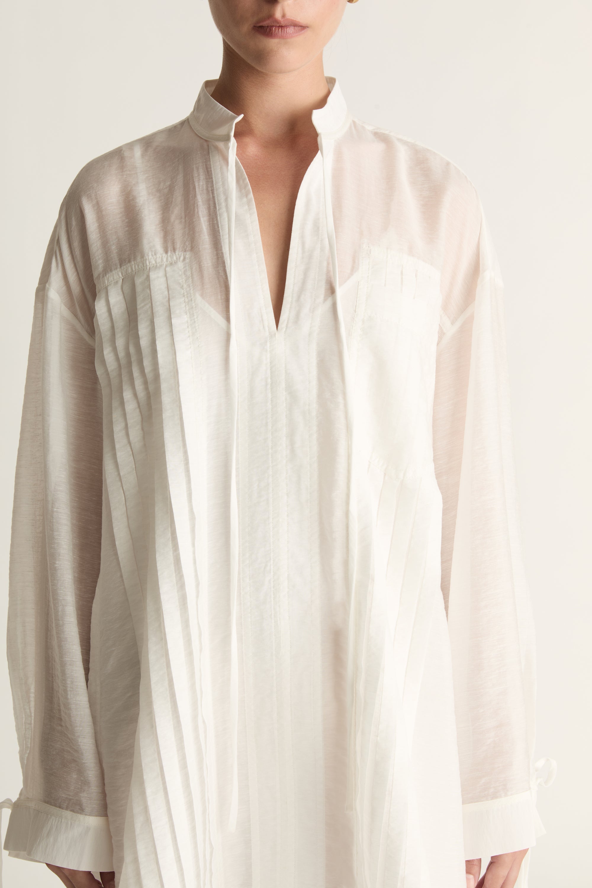 Woman wearing a white tunic against a plain background