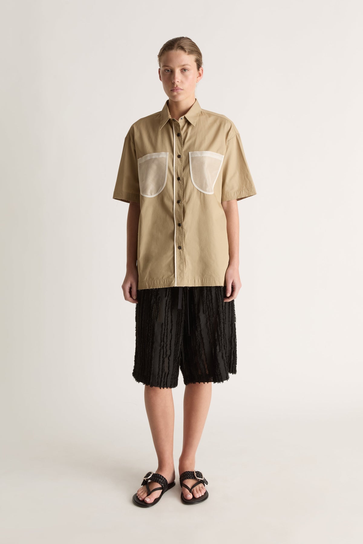 Front view of a camel short-sleeve shirt with a pointed collar, sheer chest pockets and dark buttons.