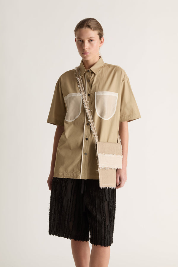 Front view of a camel short-sleeve shirt with sheer white chest pockets, worn with a cream cross-body bag.