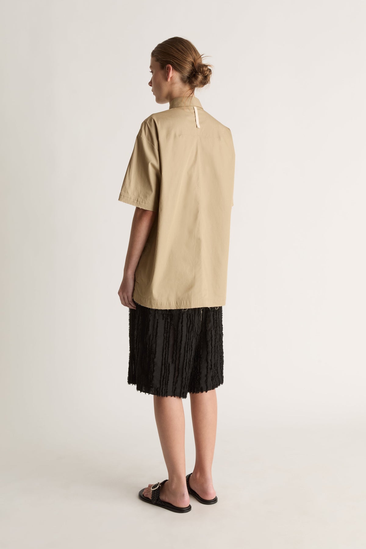 Back view of a camel short-sleeve shirt with a white loop at the back neck and a straight hem.