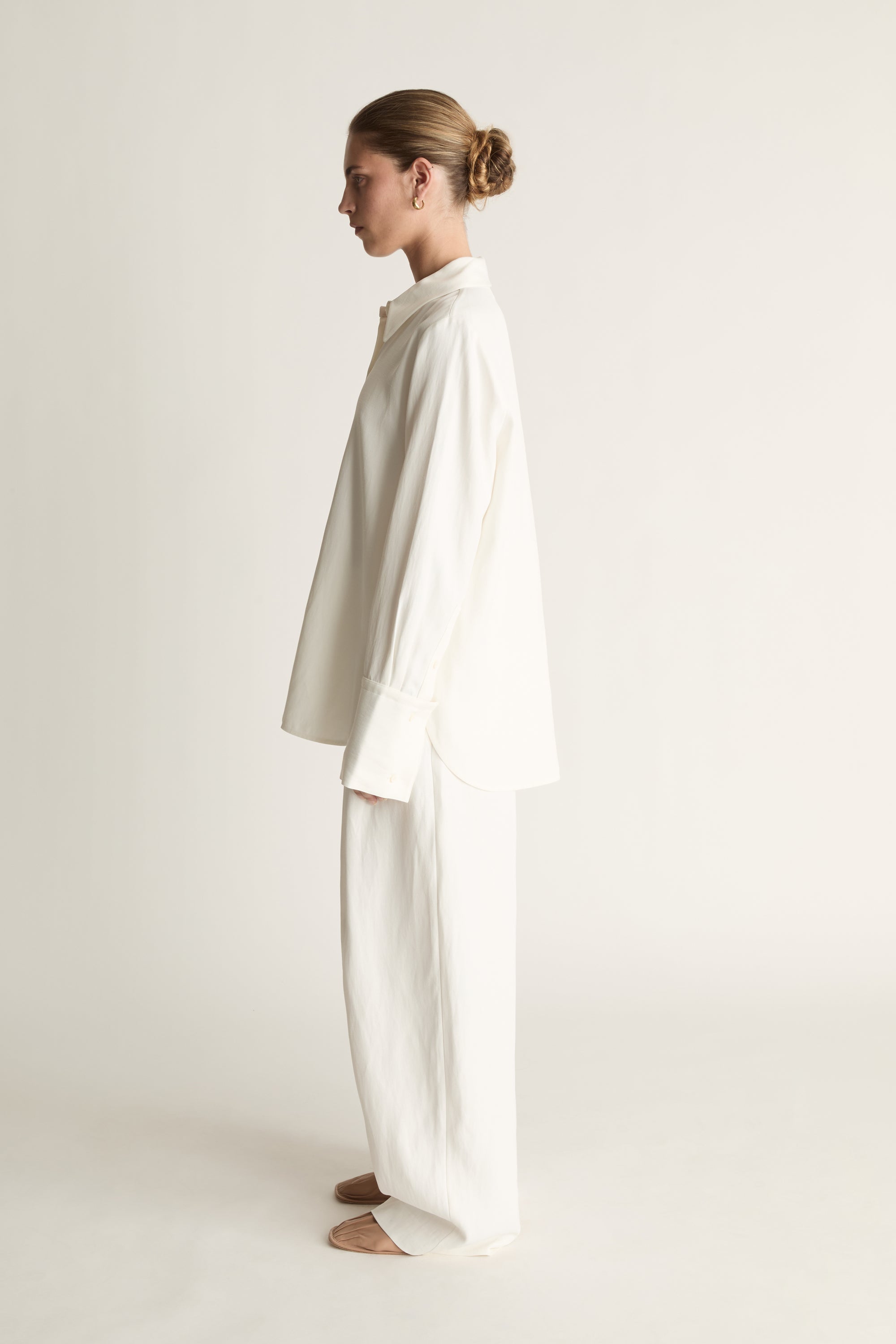 Person wearing white button up long sleeve shirt and white trousers on a pale background