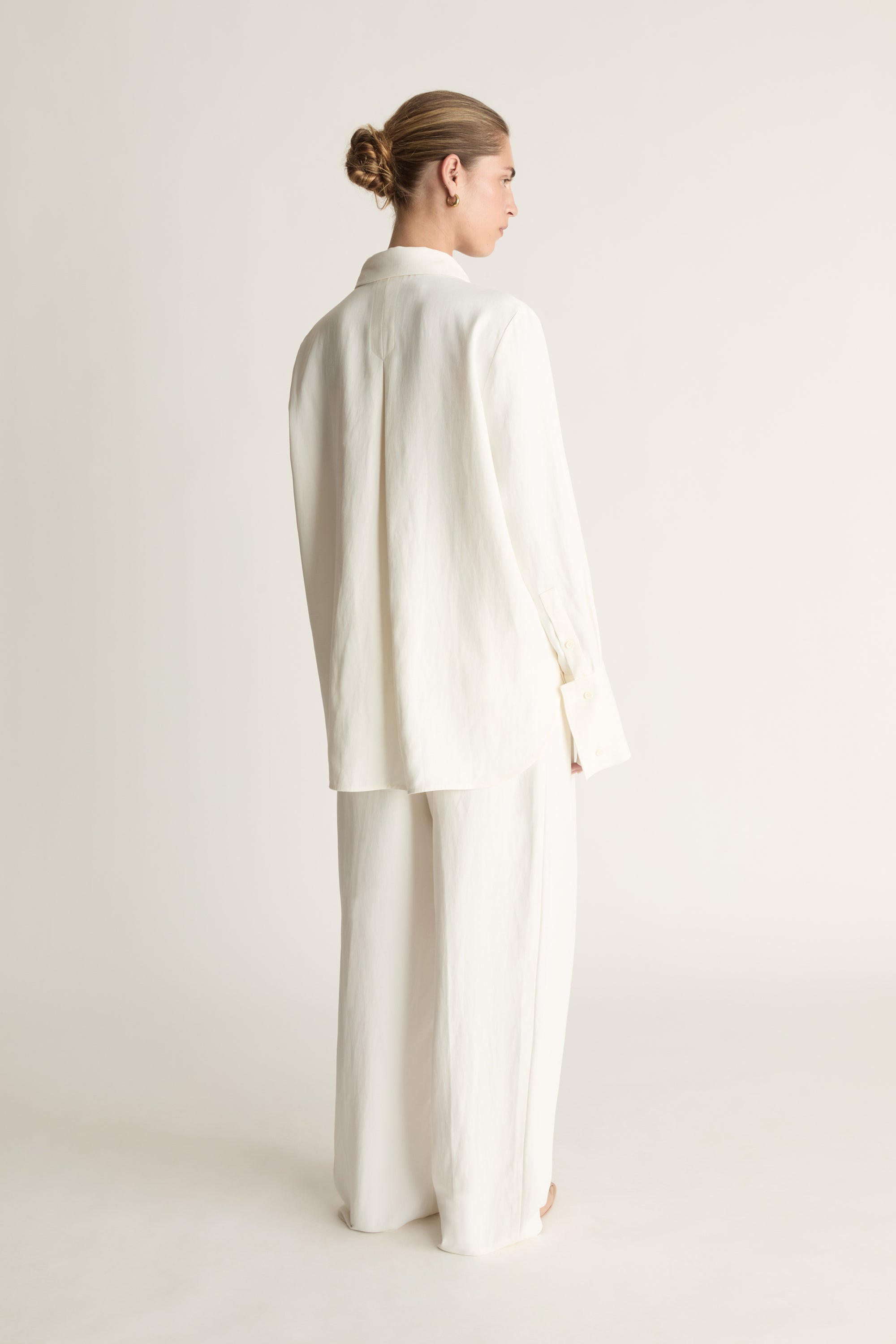 Person wearing white button up long sleeve shirt and white trousers on a pale background