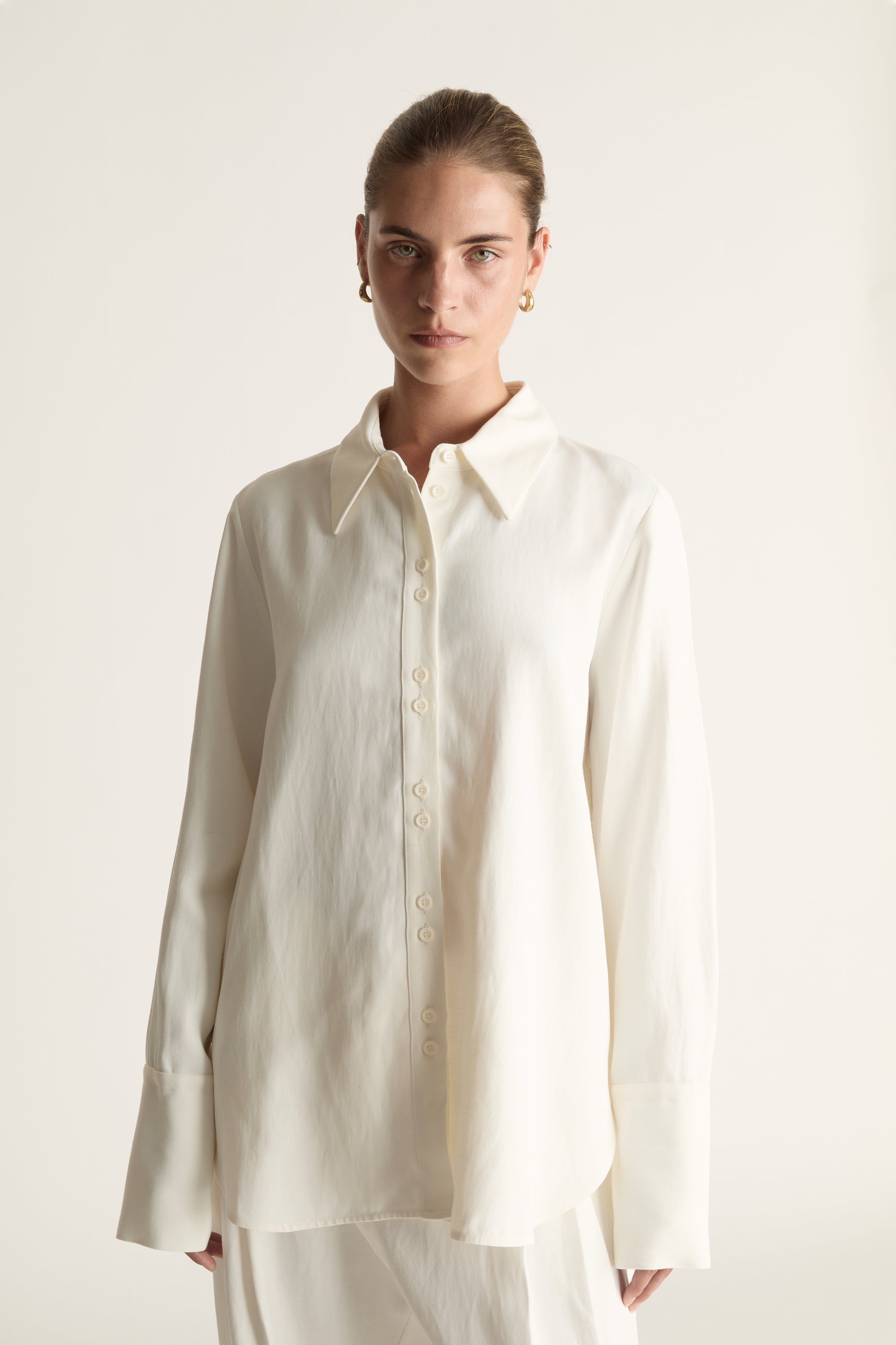 Person wearing white button up long sleeve shirt and white trousers on a pale background