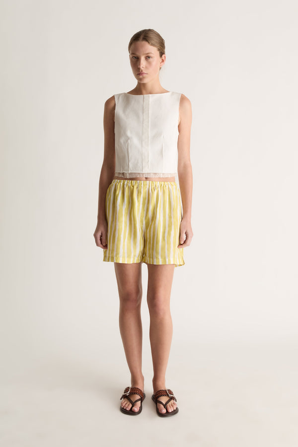 Front view of a woman wearing a white sleeveless cropped top and yellow striped silk shorts against a white studio background