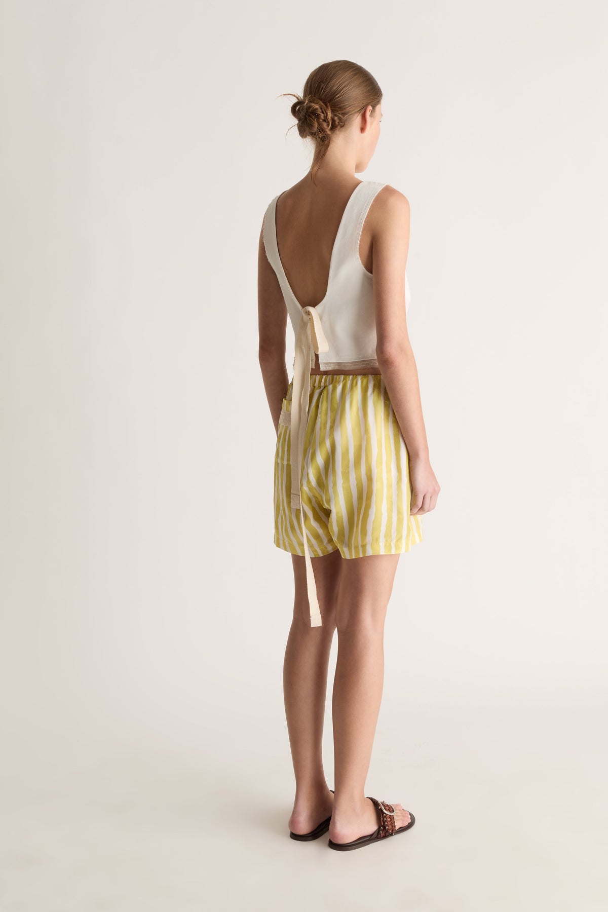 Back view of a woman with a bun in a white open-back top with long ties and yellow striped shorts