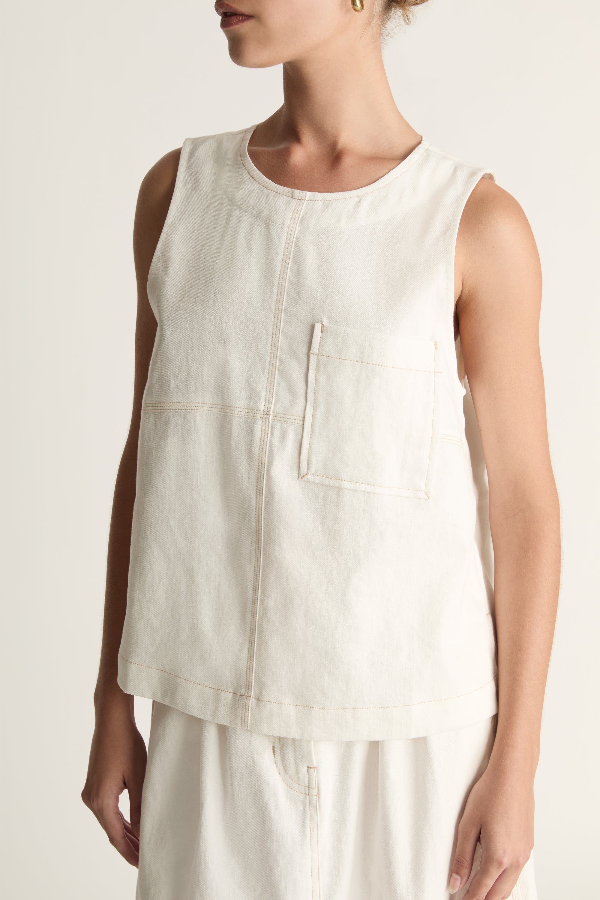 A woman wearing a white cami sleeveless tank top and a white skirt.