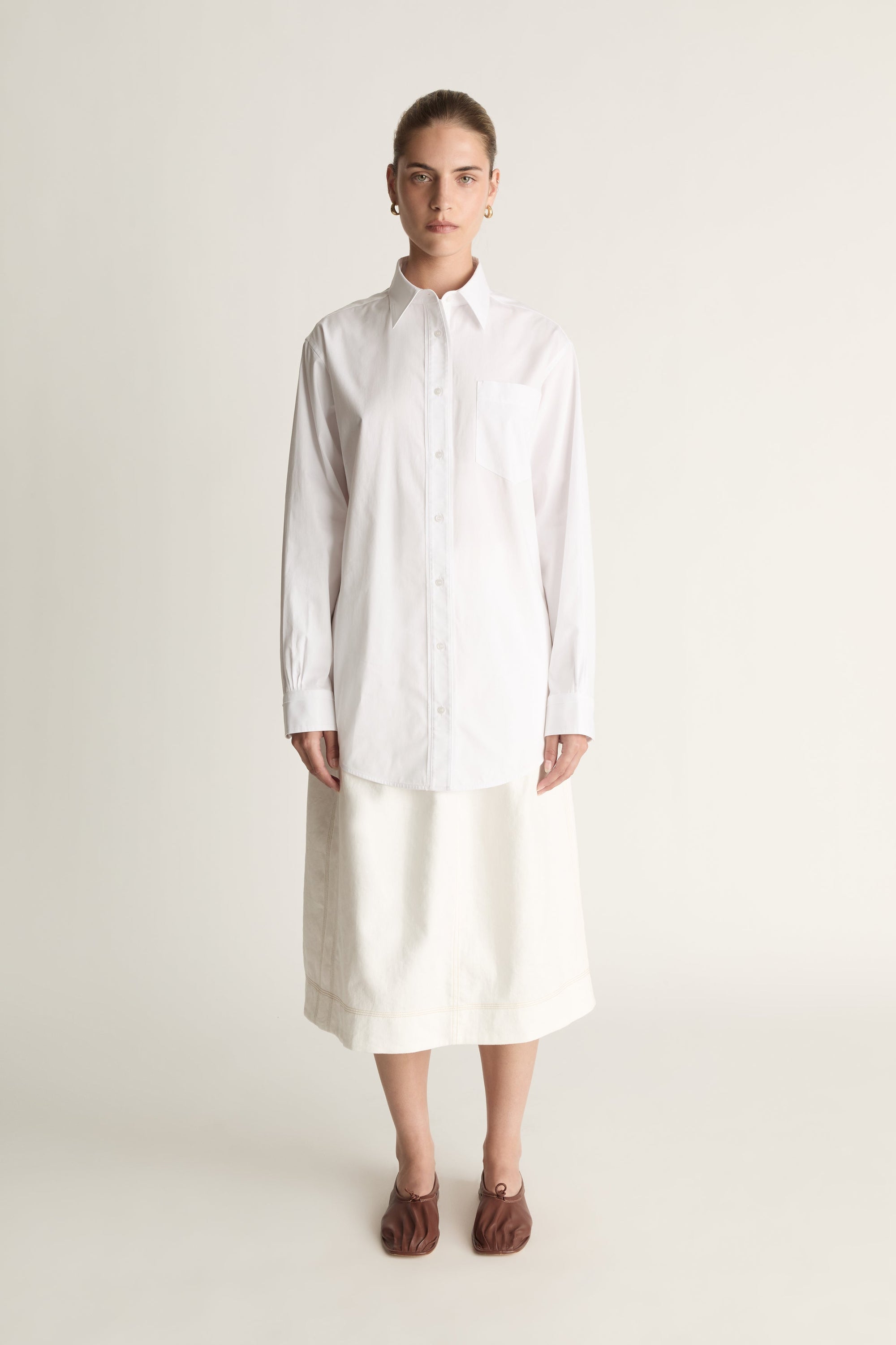 Person wearing a long white shirt and skirt on a plain background