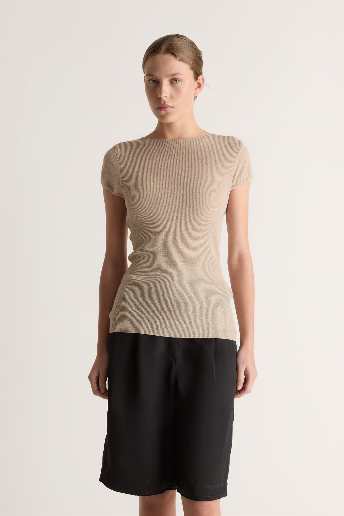 Close-up of a fitted oat knit tee with round neckline and cap sleeves, worn with black pleated shorts