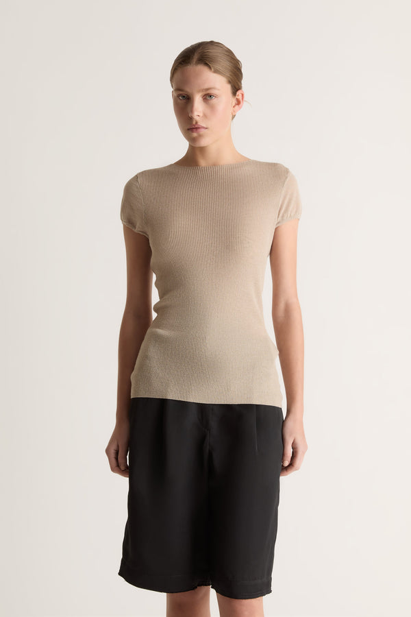 Close-up of a fitted oat knit tee with round neckline and cap sleeves, worn with black pleated shorts