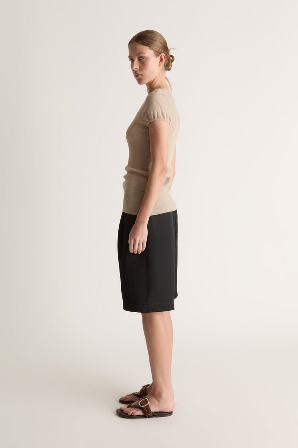 Side profile of a woman with a bun in an oat knit tee and black knee-length shorts with brown sandals