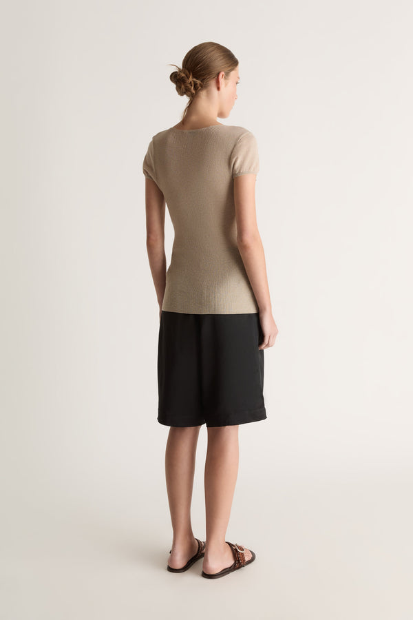 Back view of a woman with a low bun in an oat short-sleeve knit tee and black bermuda shorts