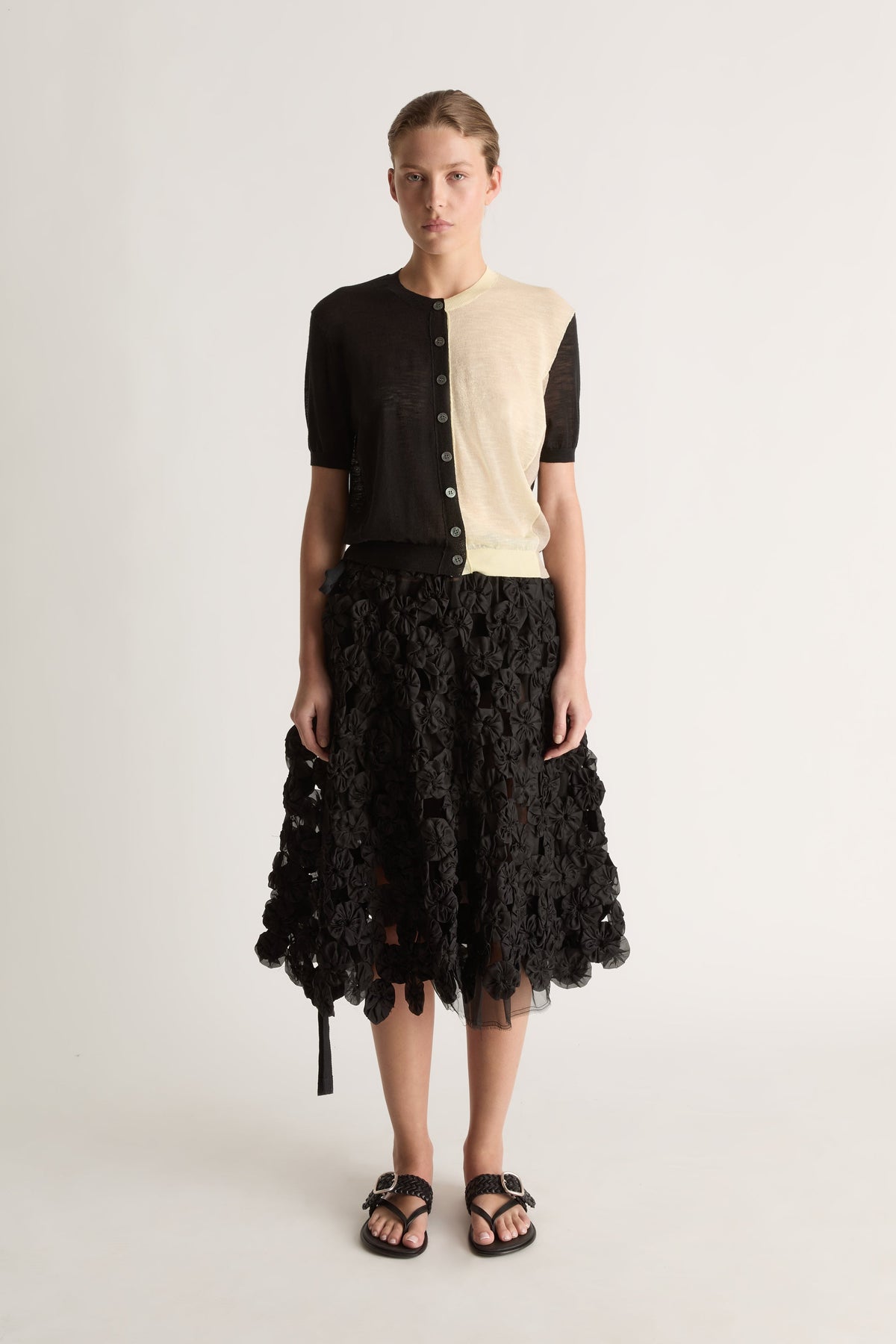 Front view of a short-sleeve button-front cardigan, black on one side and cream on the other, with ribbed trims.