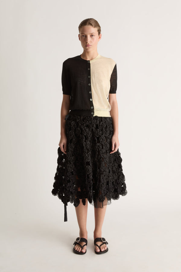 Front view of a short-sleeve button-front cardigan, black on one side and cream on the other, with ribbed trims.