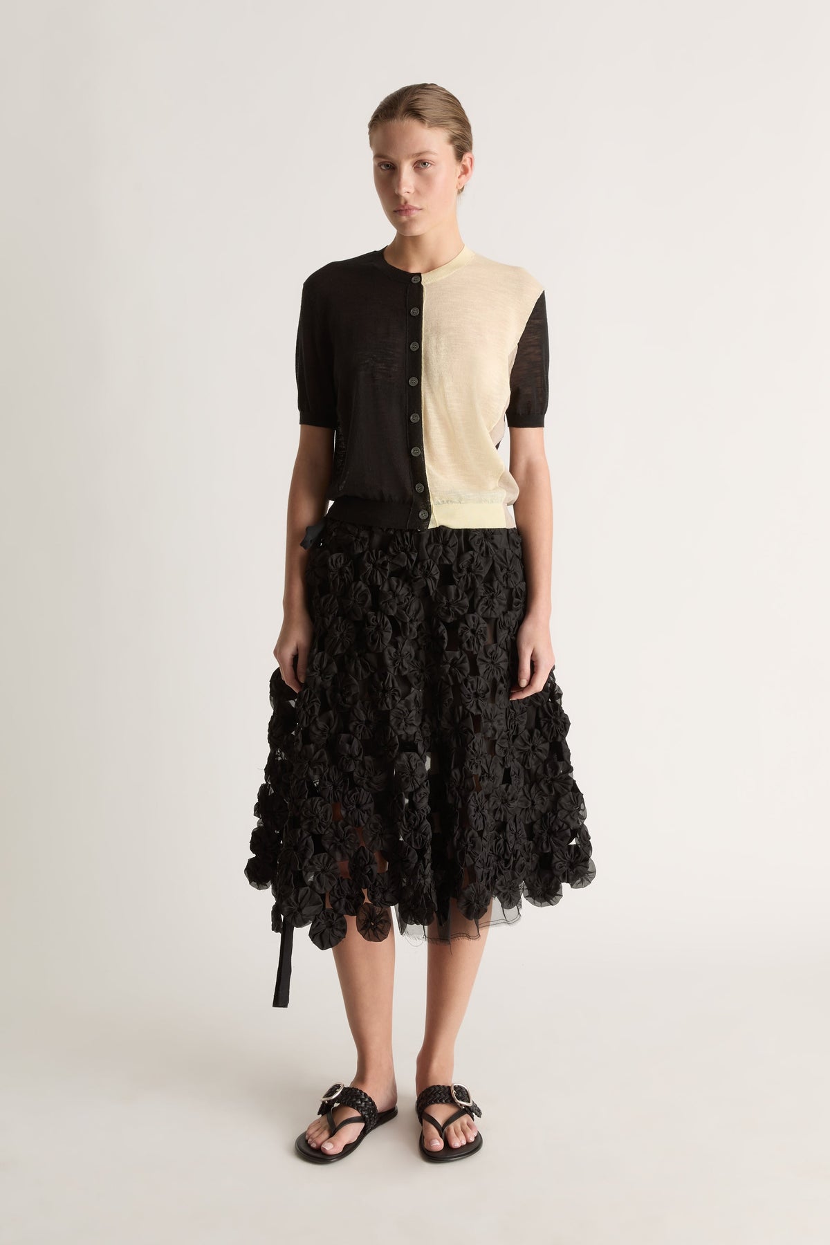 Front view of a black and cream split cardigan with short sleeves, worn with a black textured skirt.