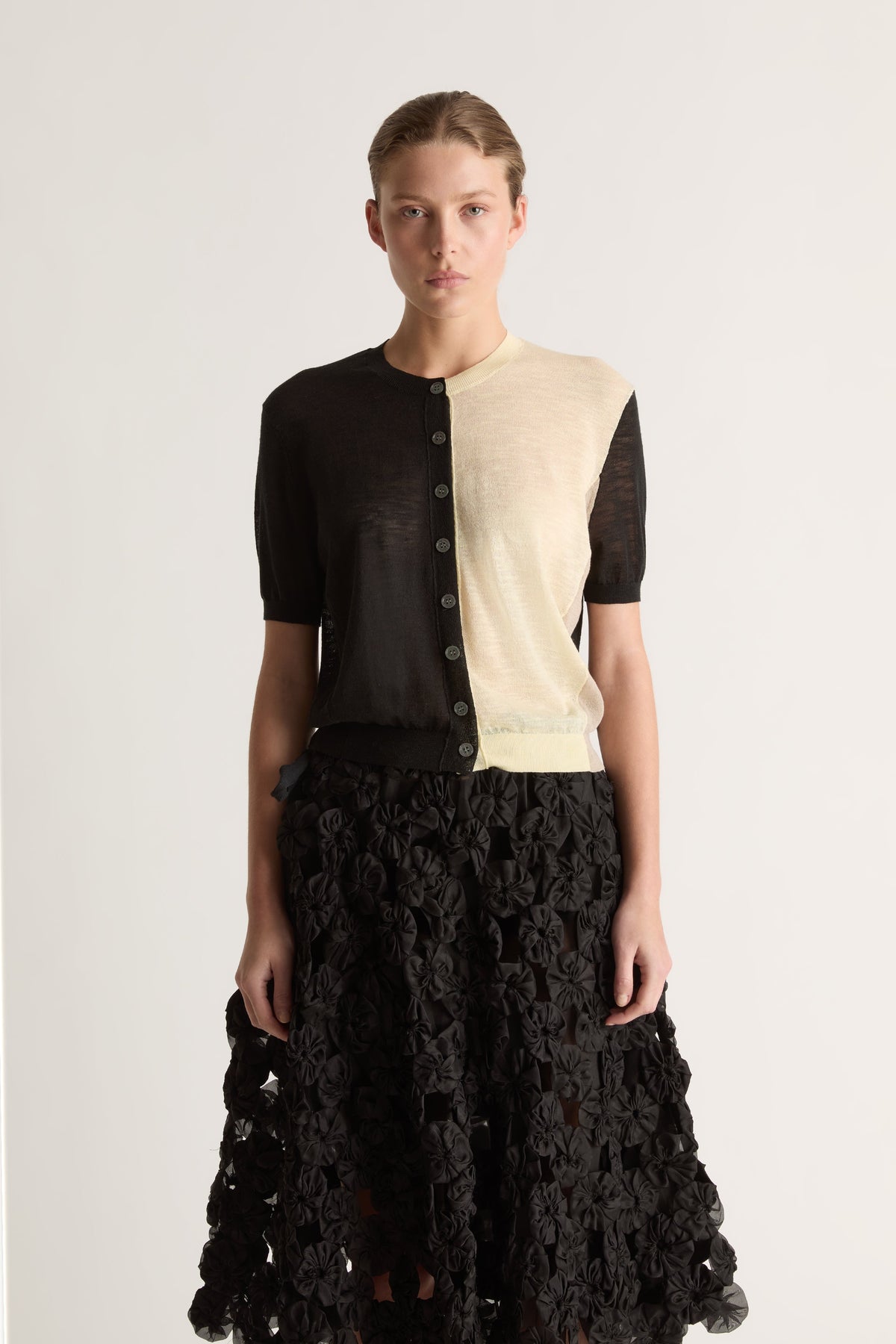 Close-up front view of a half-black, half-cream cardigan with short sleeves, round neck and dark buttons.