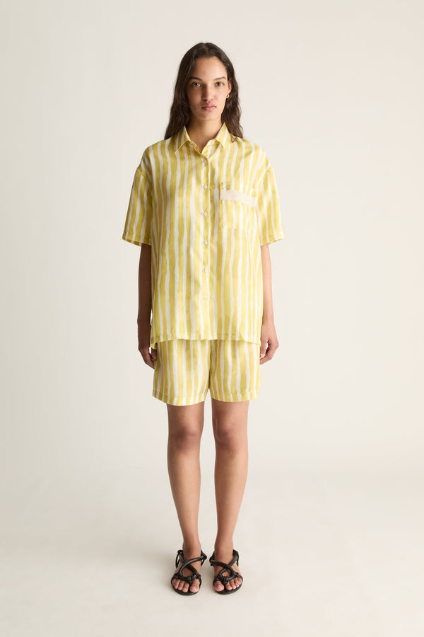 Front view of a woman wearing a yellow striped silk short-sleeve shirt and matching shorts against a white studio background