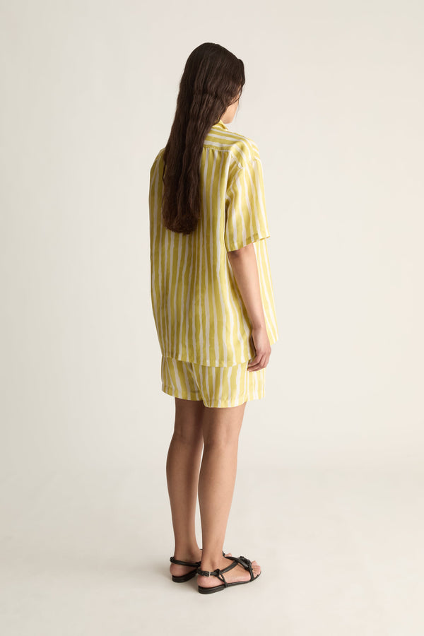 Back view of a woman with long hair in a yellow striped short-sleeve silk shirt and matching shorts