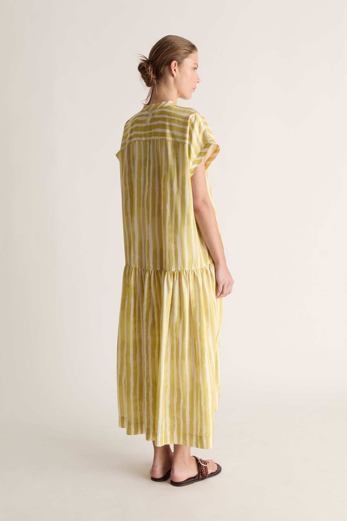 Back view of a woman with her hair up in a yellow striped silk dress with yoke seam and tiered skirt