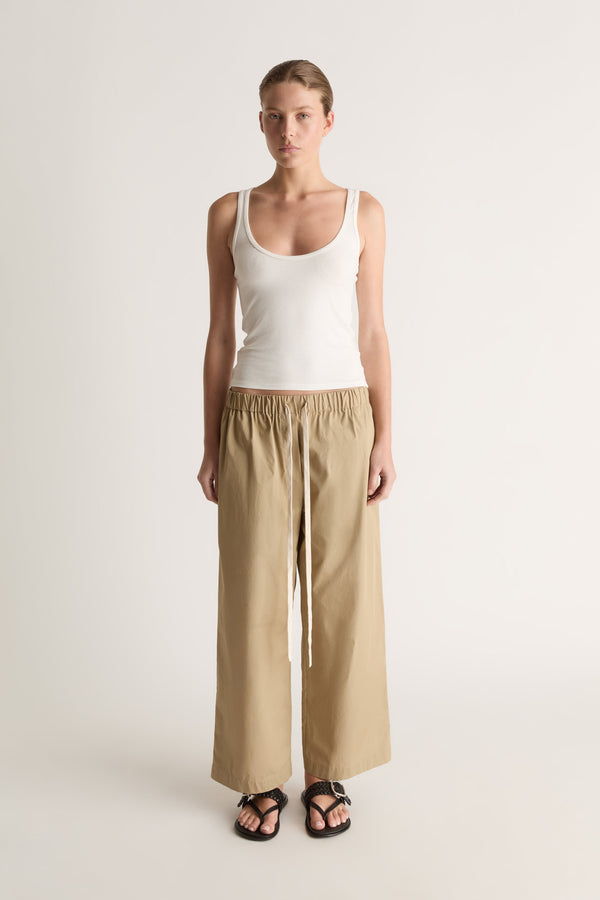 Front view of camel wide-leg pants with an elasticated waist and long cream drawstring, worn with a white tank.
