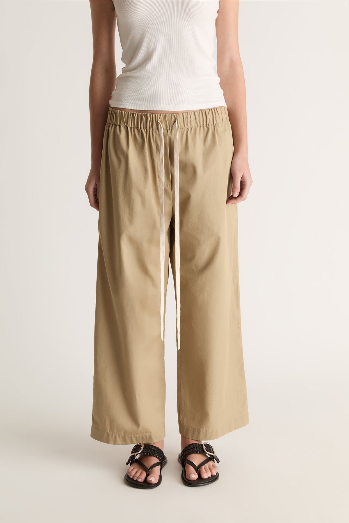 Close-up front view of camel wide-leg pants with a gathered elastic waist and long cream drawstring ties.