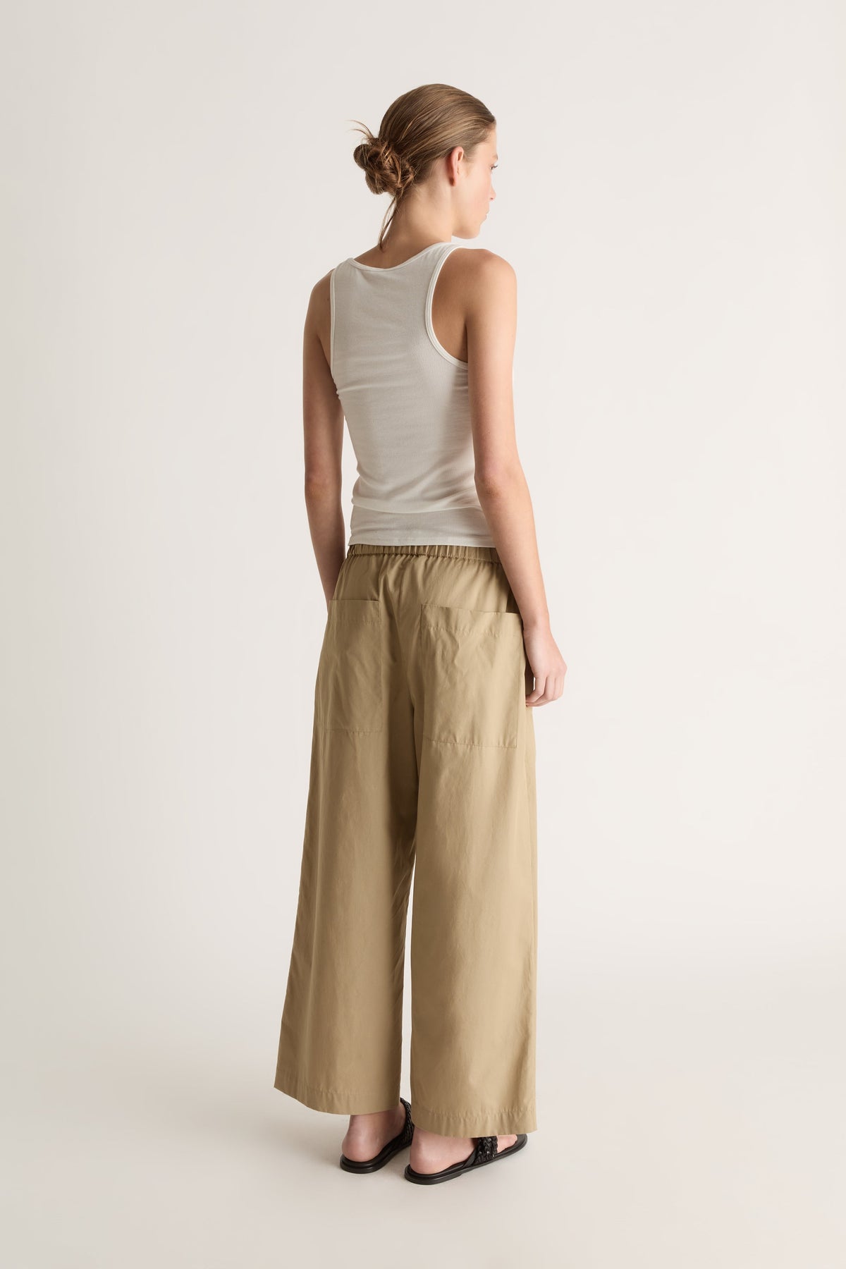 Back view of camel wide-leg pants with an elasticated waist and two back patch pockets.