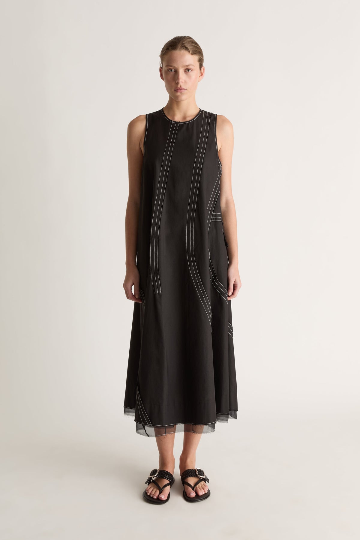 Front view of a sleeveless black midi dress with a round neck and white contrast topstitching in curved lines.