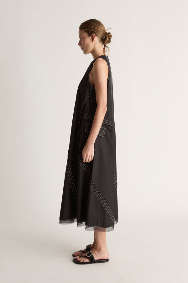 Side view of a sleeveless black midi dress with a flap pocket, white topstitching and flared hem.