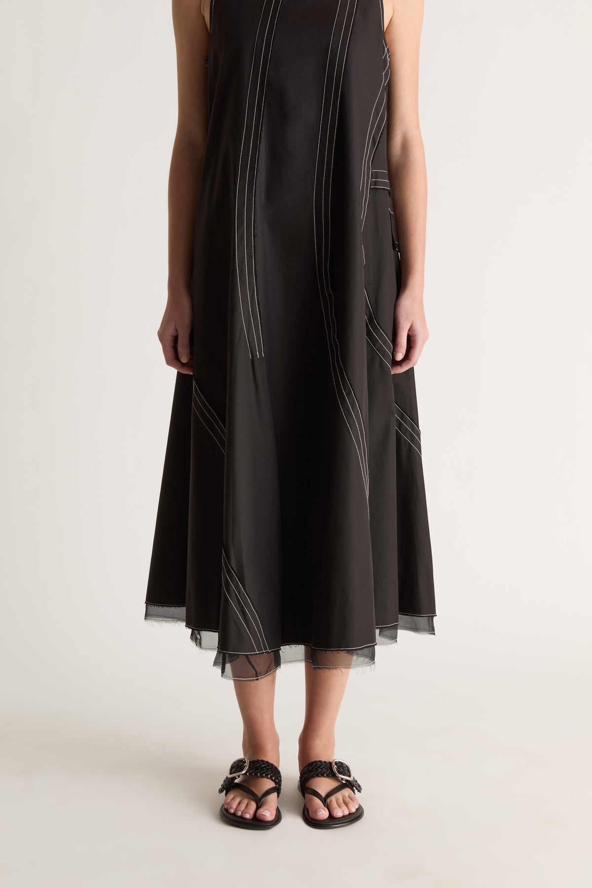 Close-up front view of a black dress skirt with white contrast topstitching and a sheer layered hem.