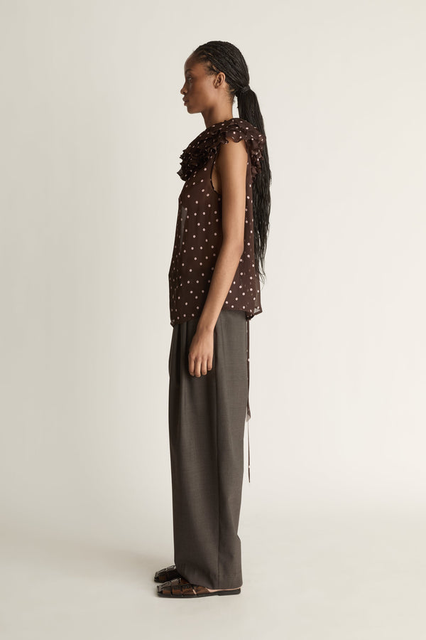 Woman wearing a brown polka dot top and dark pants on a white background