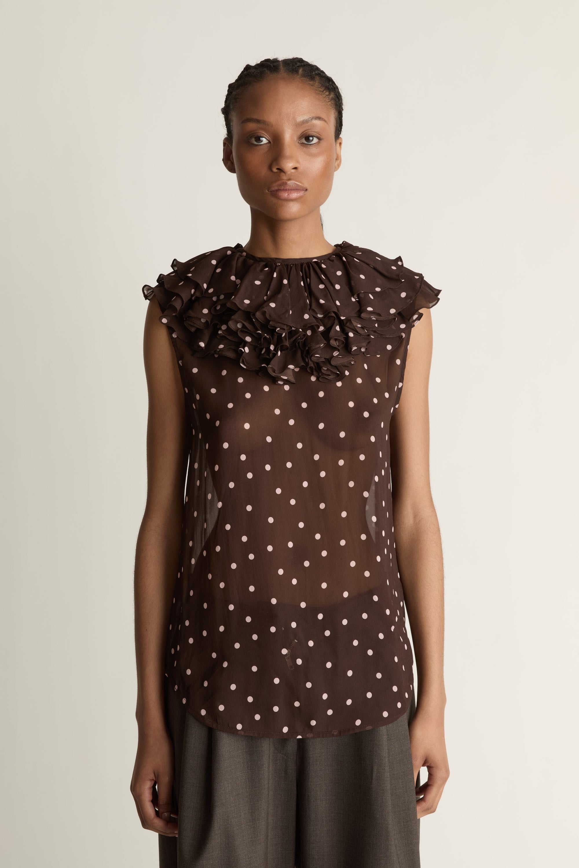 Woman wearing a brown polka dot top against a plain background