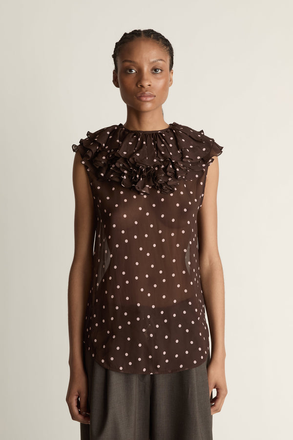 Woman wearing a brown polka dot top against a plain background