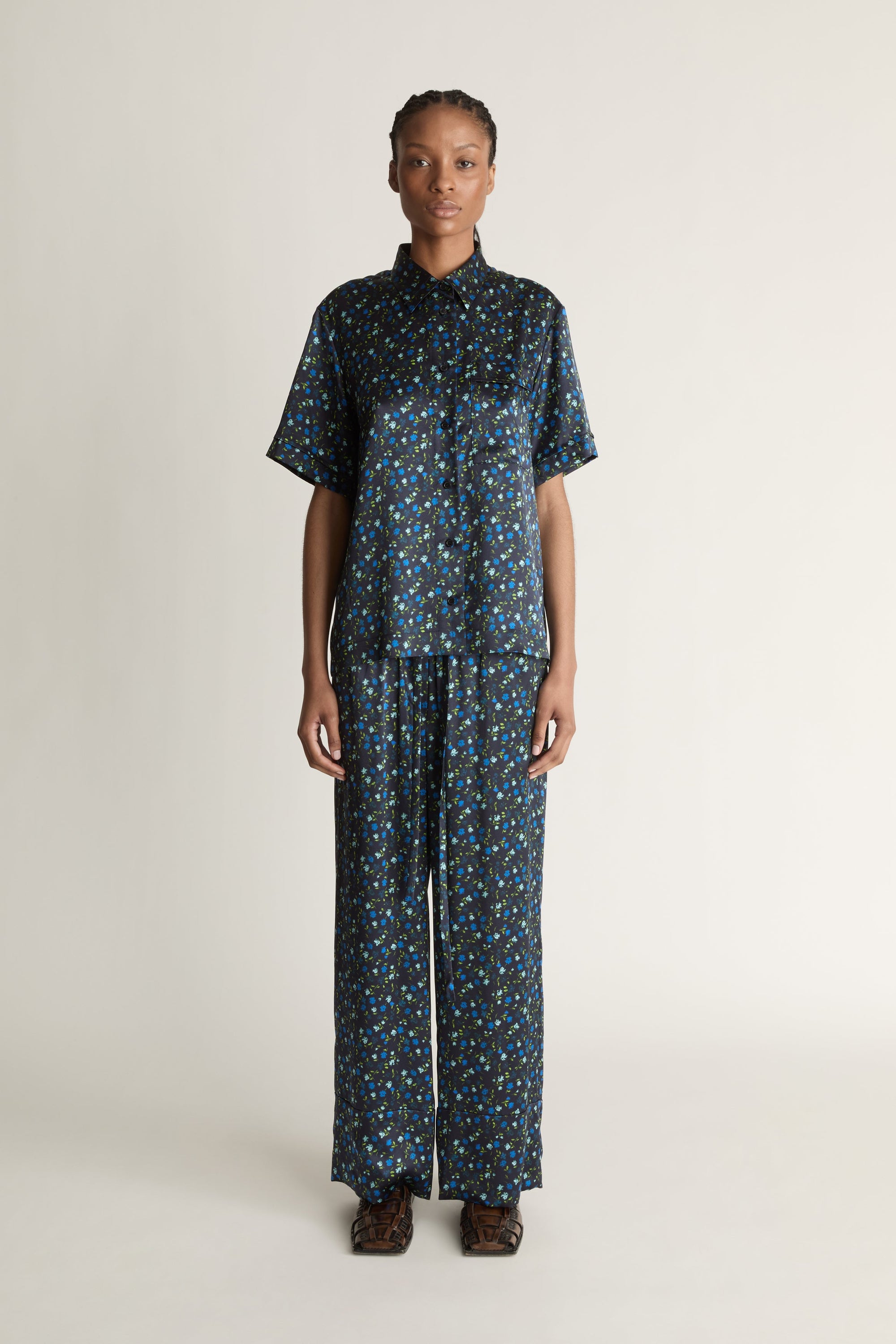 Person wearing a blue printed button-up shirt and pants on a plain background