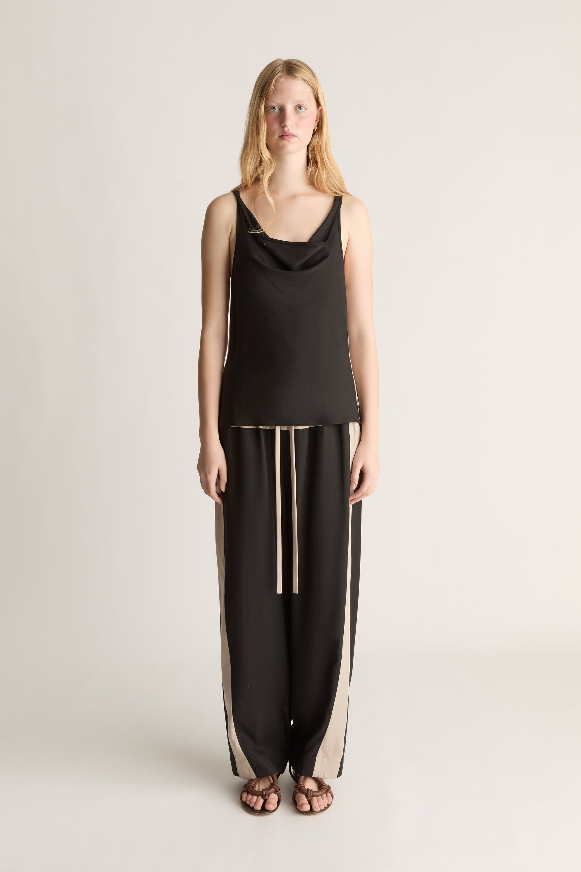 Woman wearing a black sleeveless top and pants on a plain background