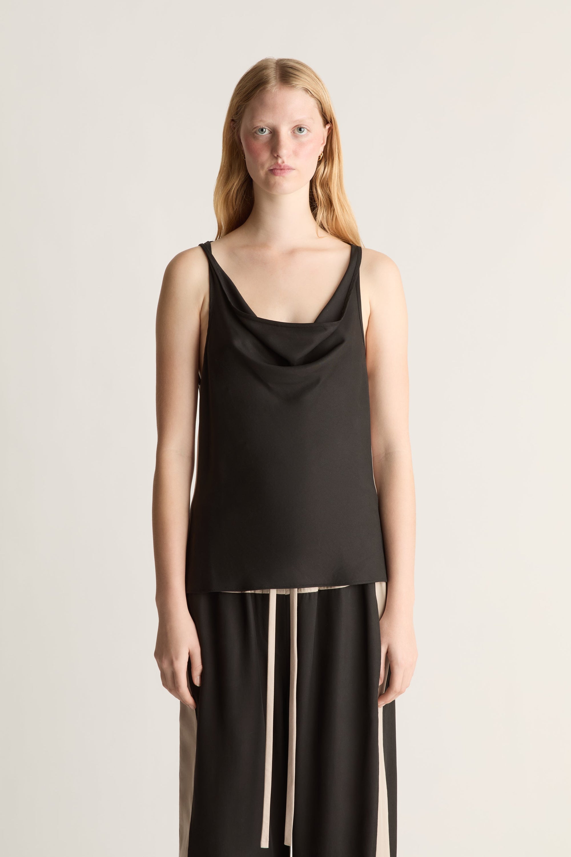 Woman wearing a black sleeveless top and pants on a plain background