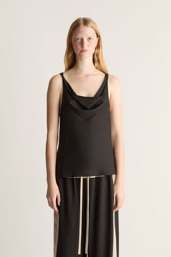Woman wearing a black sleeveless top and pants on a plain background