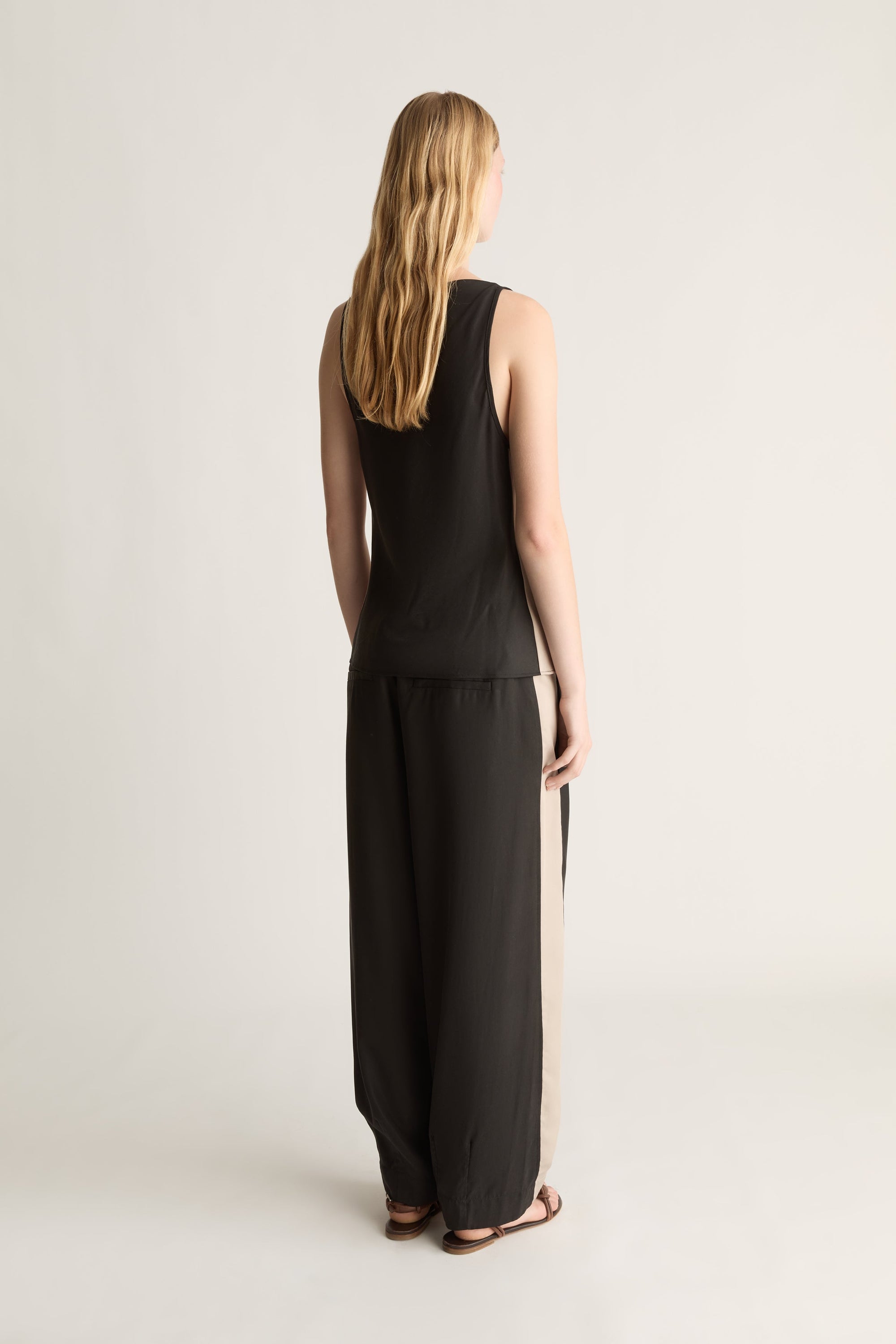 Woman wearing a black sleeveless top and pants on a plain background