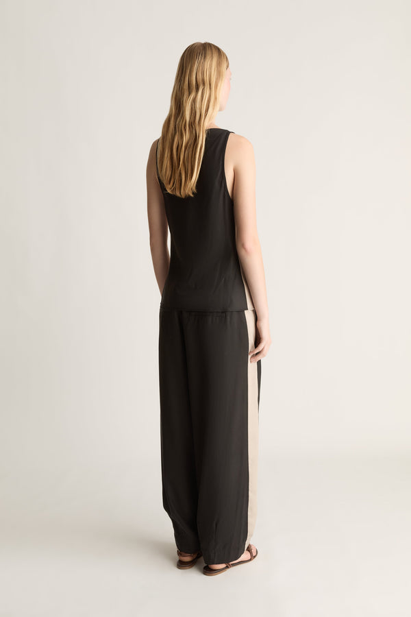 Woman wearing a black sleeveless top and pants on a plain background
