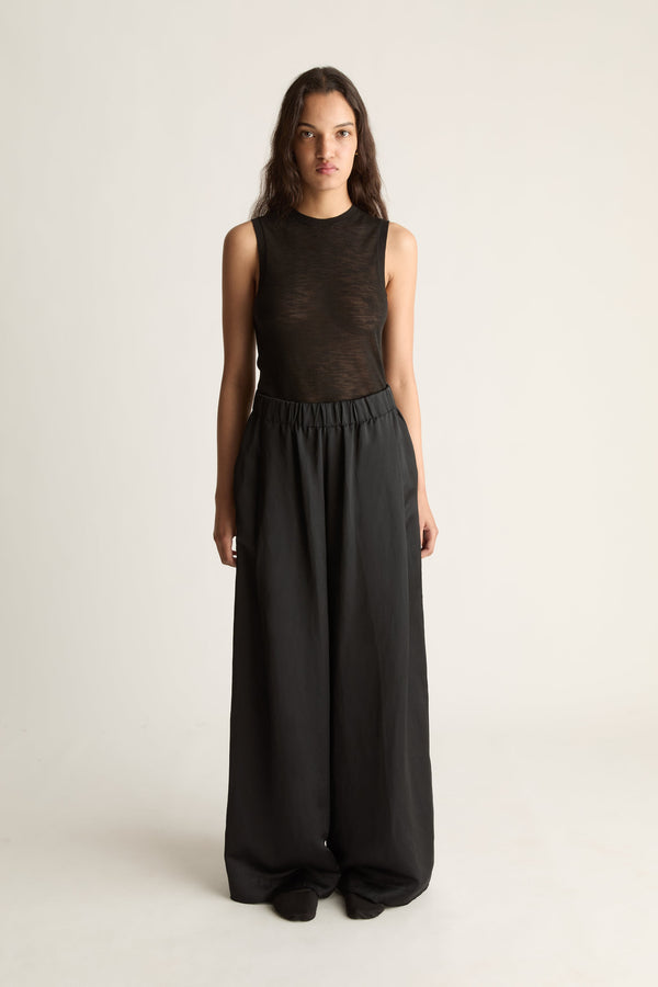 Front view of a woman wearing a black knit top and wide-leg elastic-waist pants against a white studio background